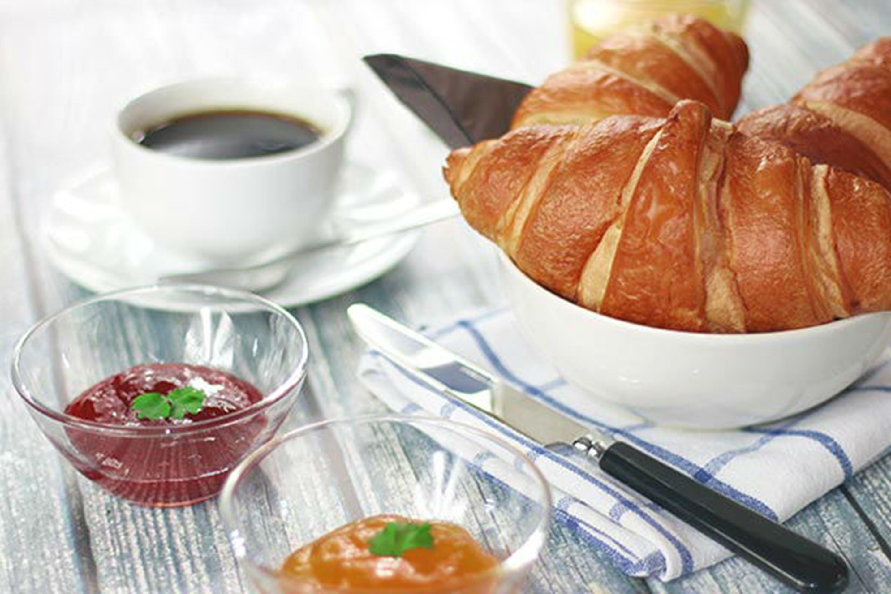 Un tavolo con croissant, una tazza di caffè e due piccole ciotole di marmellata.