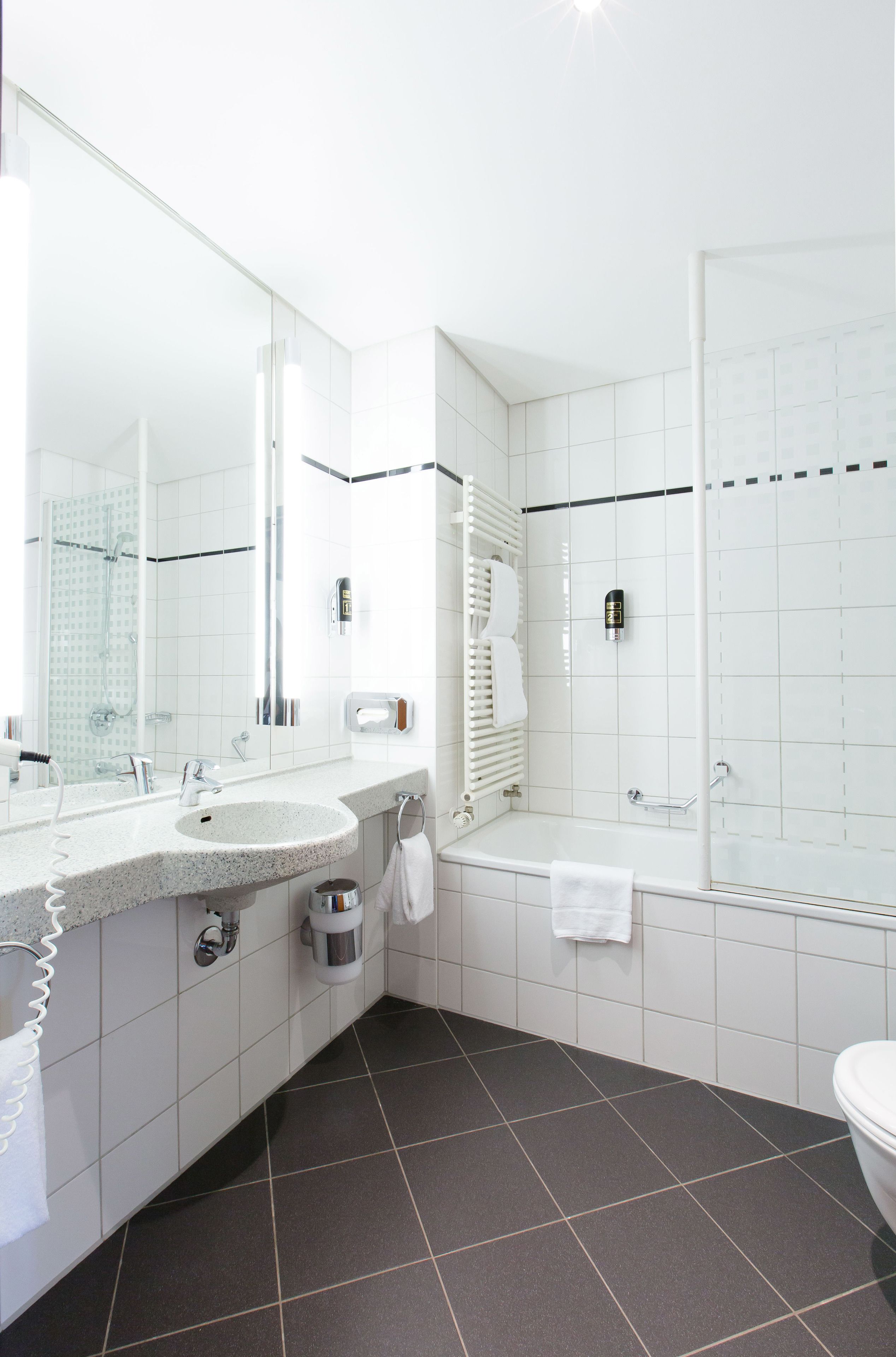 A modern bathroom with a large mirror, a sink, a bathtub, and a toilet.