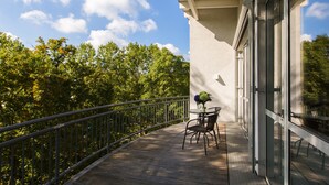 Un balcon avec une table et des chaises, donnant sur un paysage verdoyant et luxuriant et sur un ciel bleu azur.
