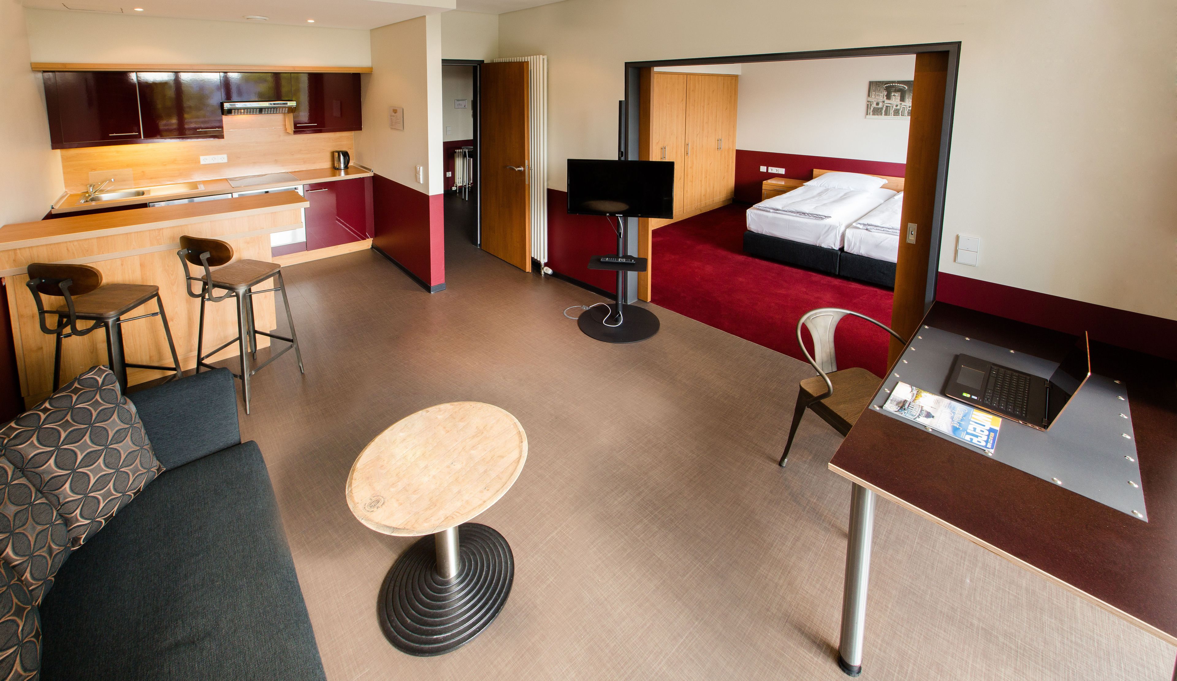 Habitación de hotel compacta con kitchenette, un pequeño comedor, un sofá, una cama individual y un televisor.