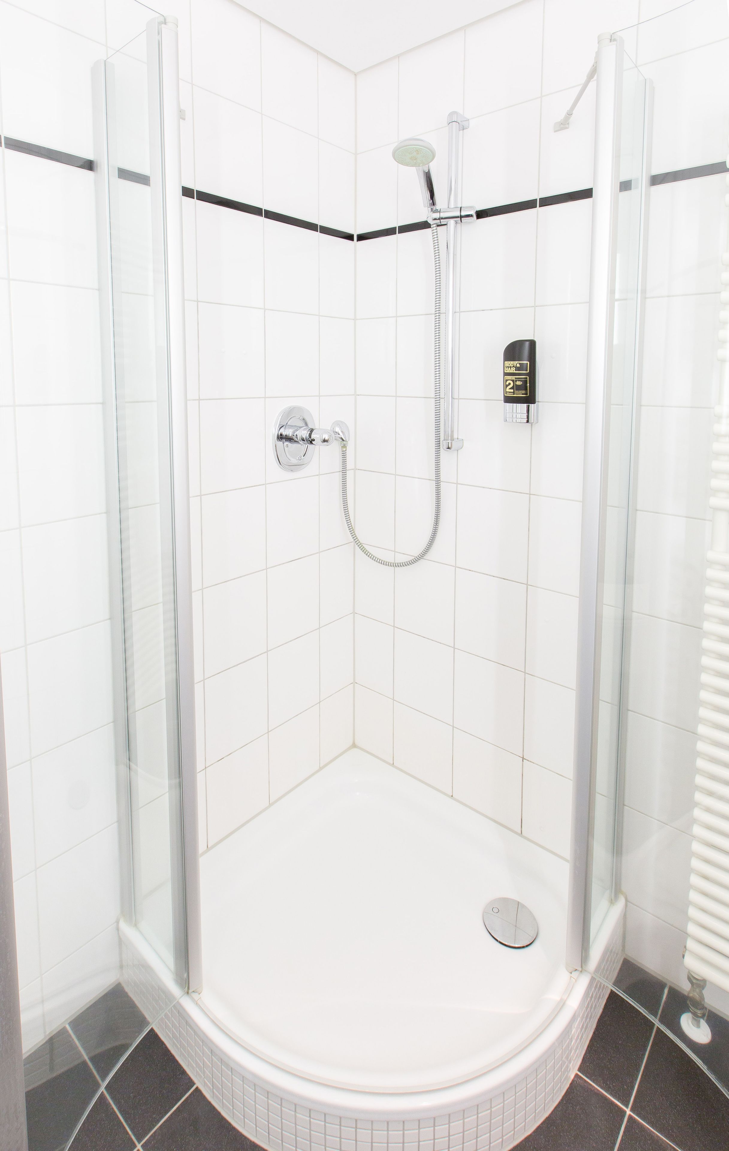 Een glazen douchecabine met een handdouche, een bedieningspaneel aan de muur en een betegeld hoekontwerp.