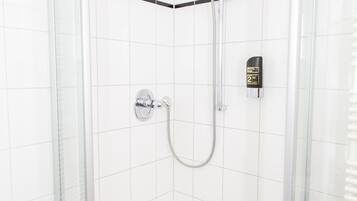 Een glazen douchecabine met een handdouche, een bedieningspaneel aan de muur en een betegeld hoekontwerp.
