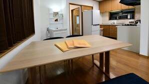 A compact kitchen with a microwave, stove, and refrigerator. There is a dining table with chairs and a bench.
