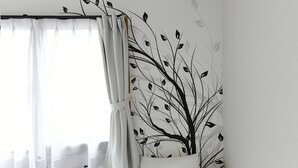 A bedroom with a bed, white curtains, and a wall with a black tree design.