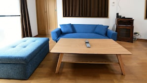 A room with a blue sofa, a matching ottoman, and a wooden coffee table with a remote control on it.