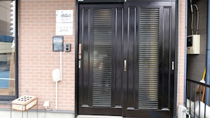 A dark wooden door with a sign above it, a brick wall, and a small electrical box on the left.