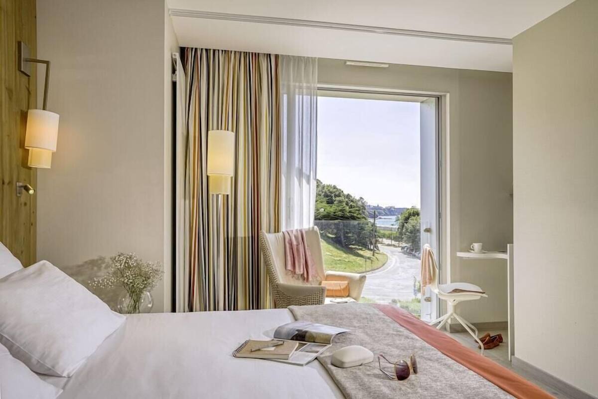 Une chambre d’hôtel avec un lit, une chaise, une petite table et une vue sur un paysage.