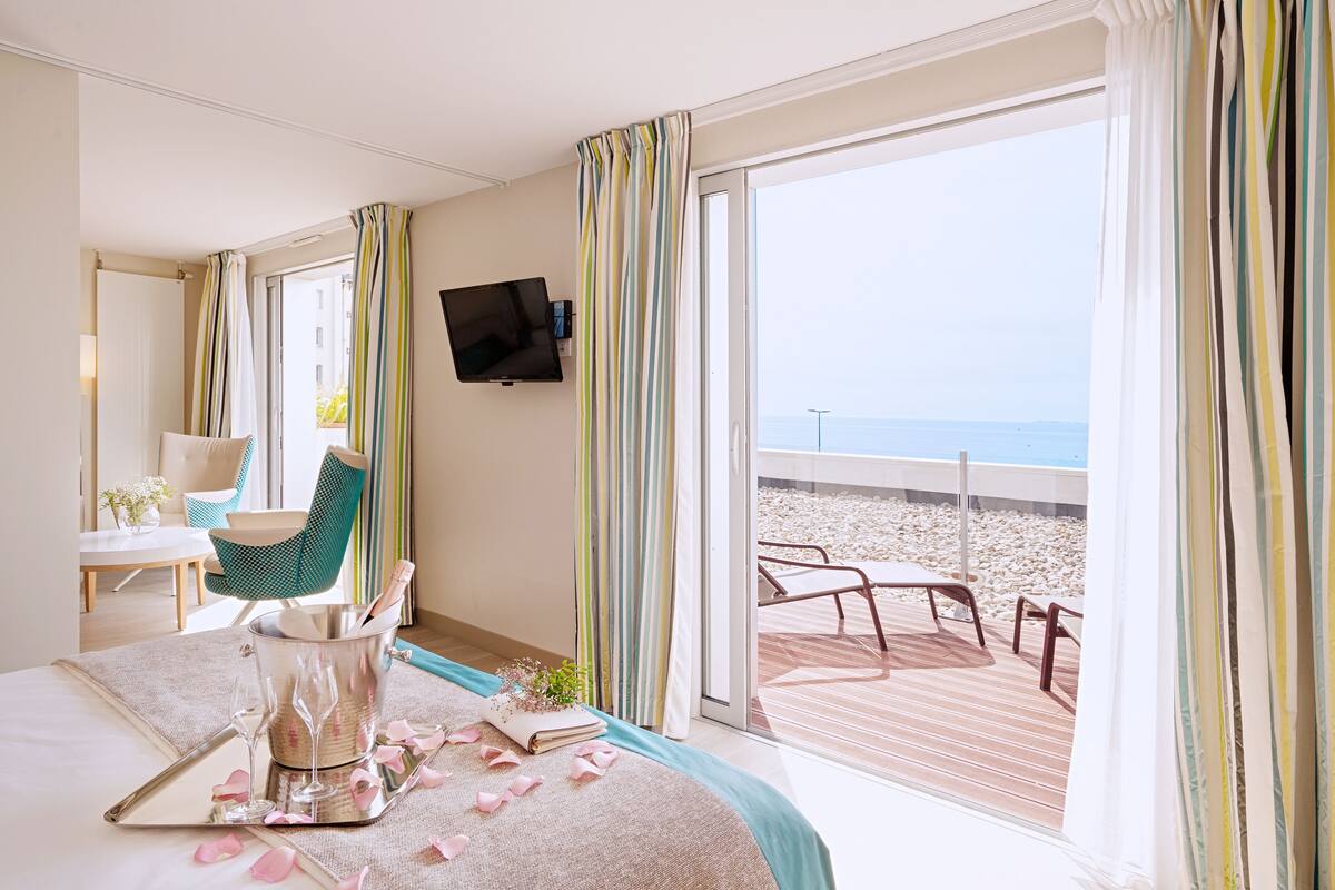 Une chambre d’hôtel comprenant un lit, une télévision, un coin repas et un balcon avec vue sur la plage.
