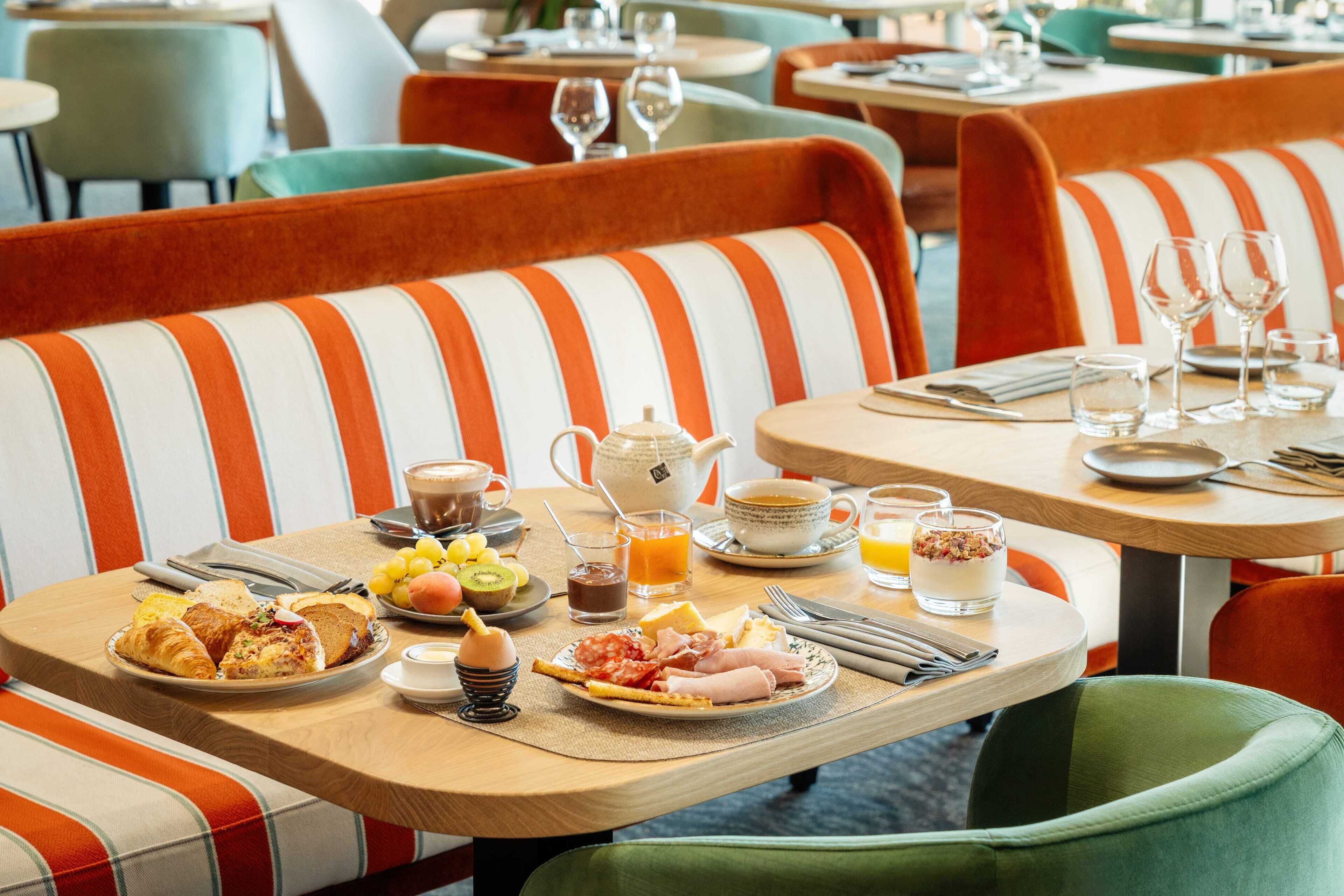 A breakfast setting with striped orange and white upholstered chairs, a table set with croissants, fruits, eggs, and beverages.