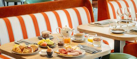 A breakfast setting with striped orange and white upholstered chairs, a table set with croissants, fruits, eggs, and beverages.