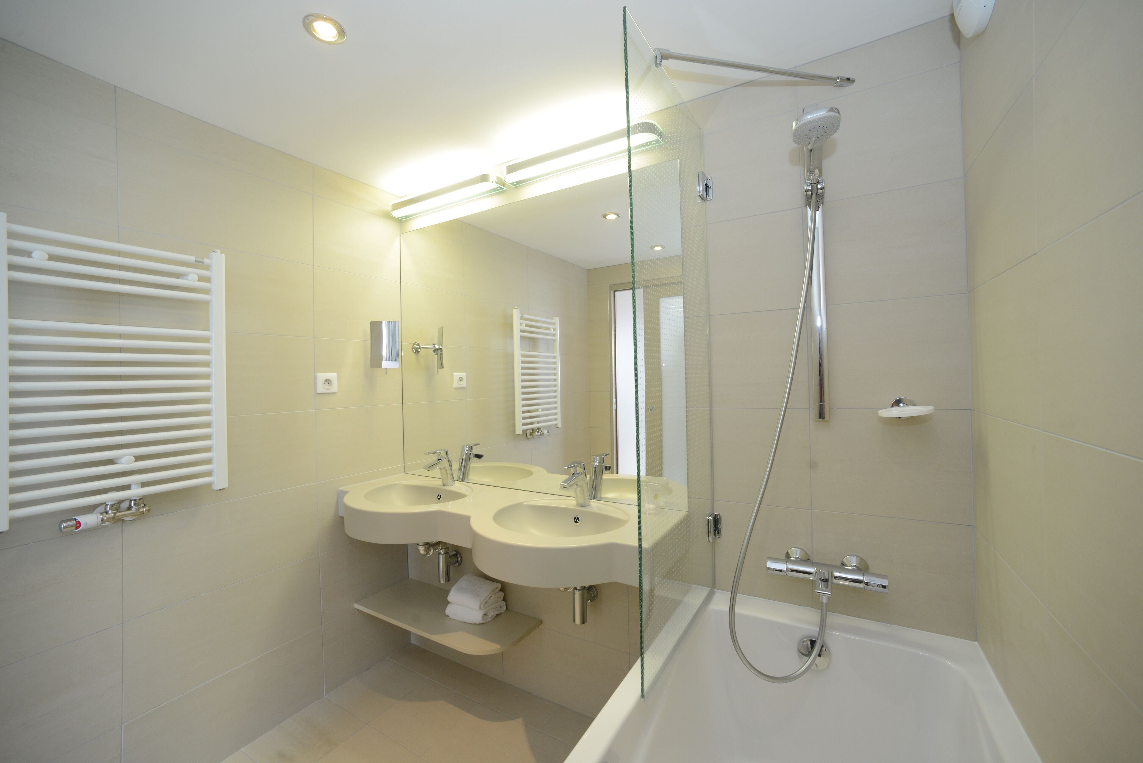 A modern bathroom with two sinks, a glass shower enclosure, and a bathtub.