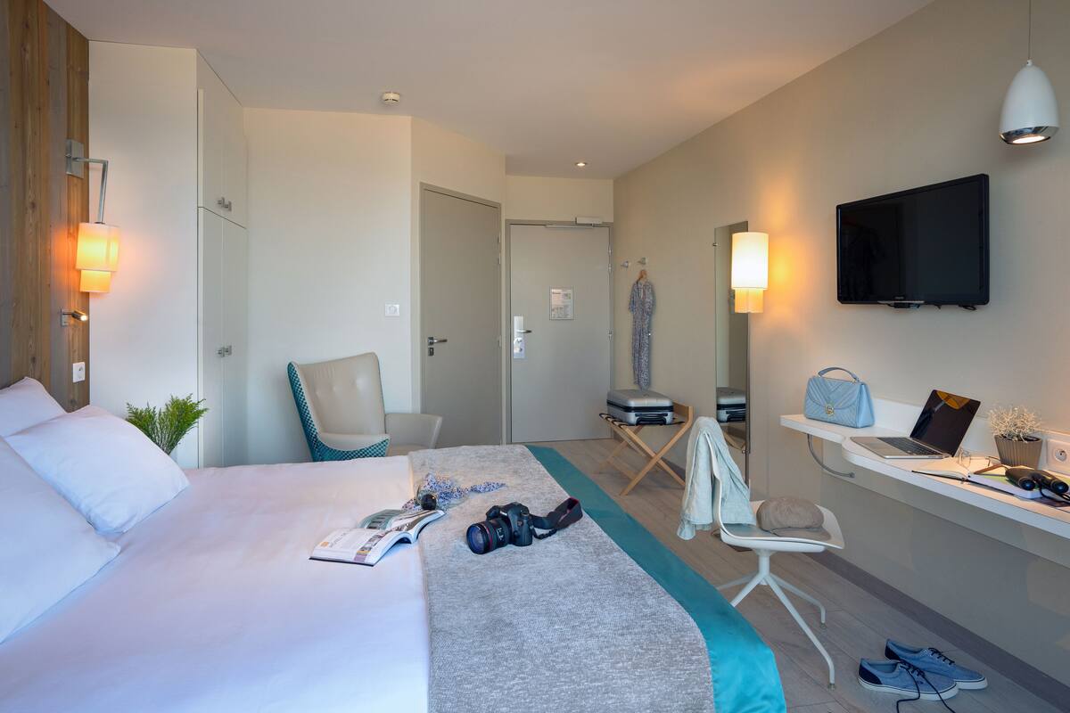 Une chambre d’hôtel moderne équipée d’un lit, d’un bureau avec un ordinateur portable, d’une chaise, d’une télévision et d’une armoire.
