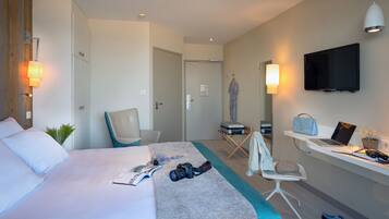 Ein modernes Hotelzimmer mit einem Bett, einem Schreibtisch mit einem Laptop, einem Sessel, einem Fernseher und einem Kleiderschrank.