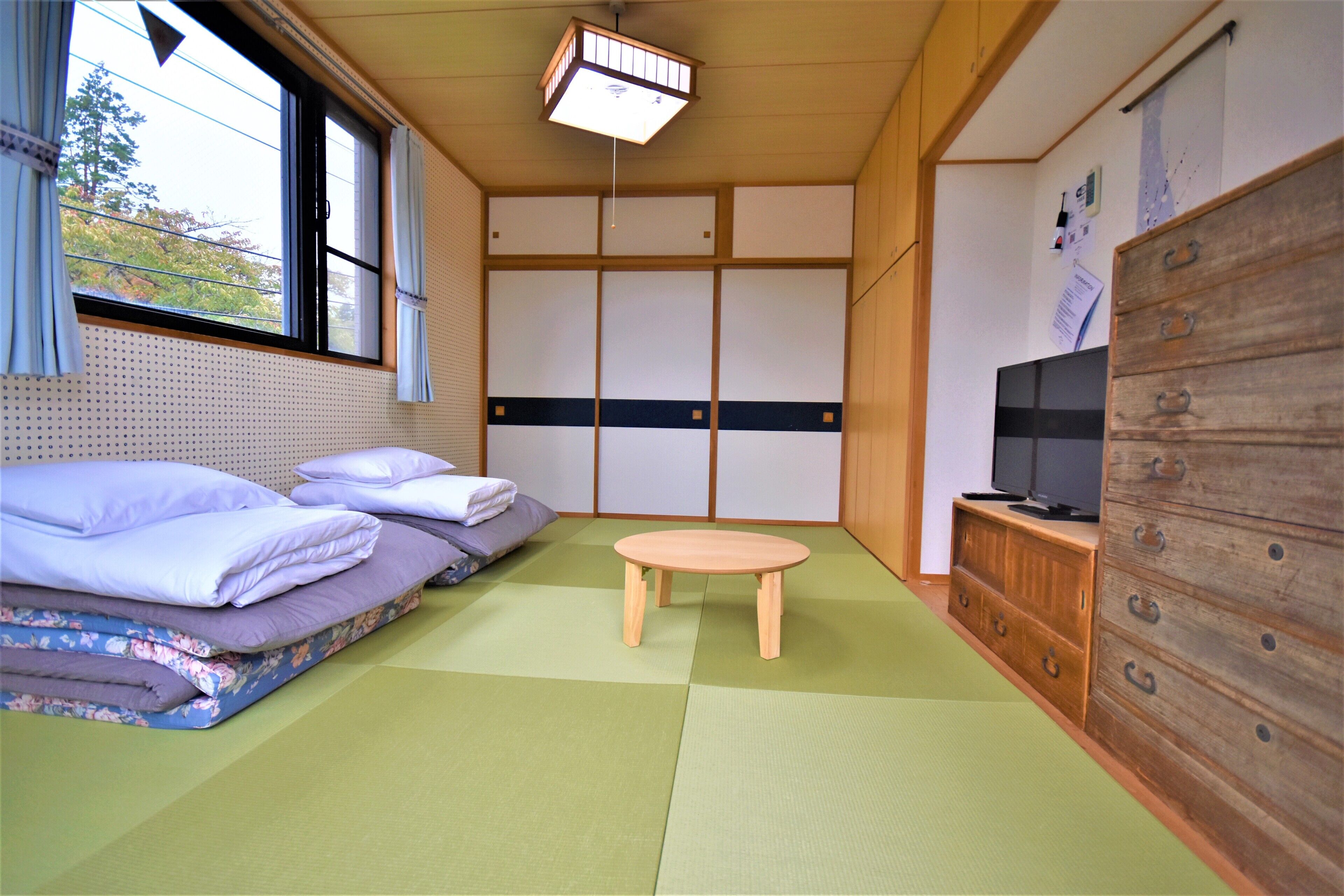 A traditional Japanese-style room with tatami flooring, a futon bed, a small wooden table, and a TV on a wooden cabinet.