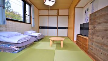 A traditional Japanese-style room with tatami flooring, a futon bed, a small wooden table, and a TV on a wooden cabinet.