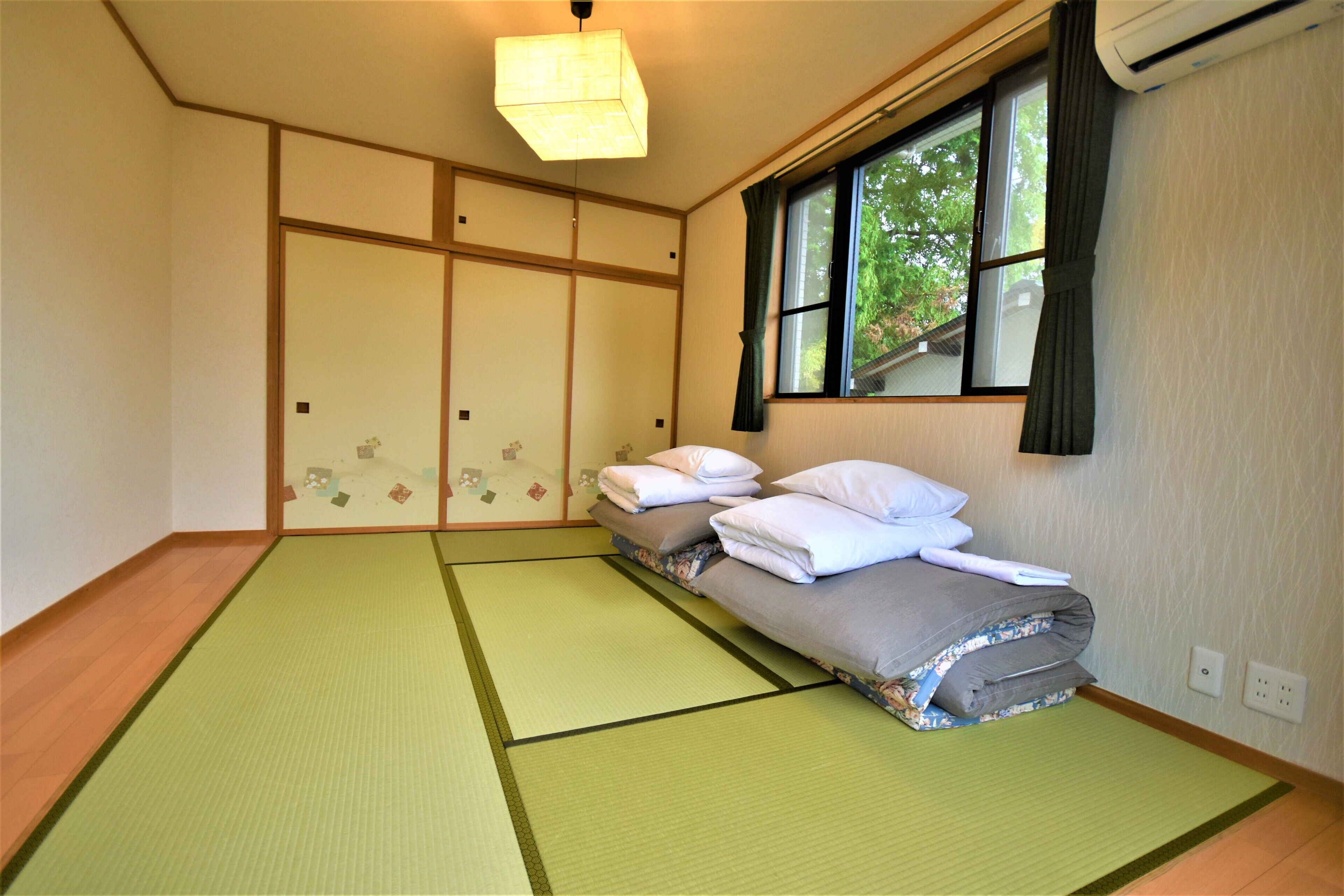 Una camera tradizionale giapponese con tatami, un letto basso, porte scorrevoli e una finestra con vista sugli alberi.