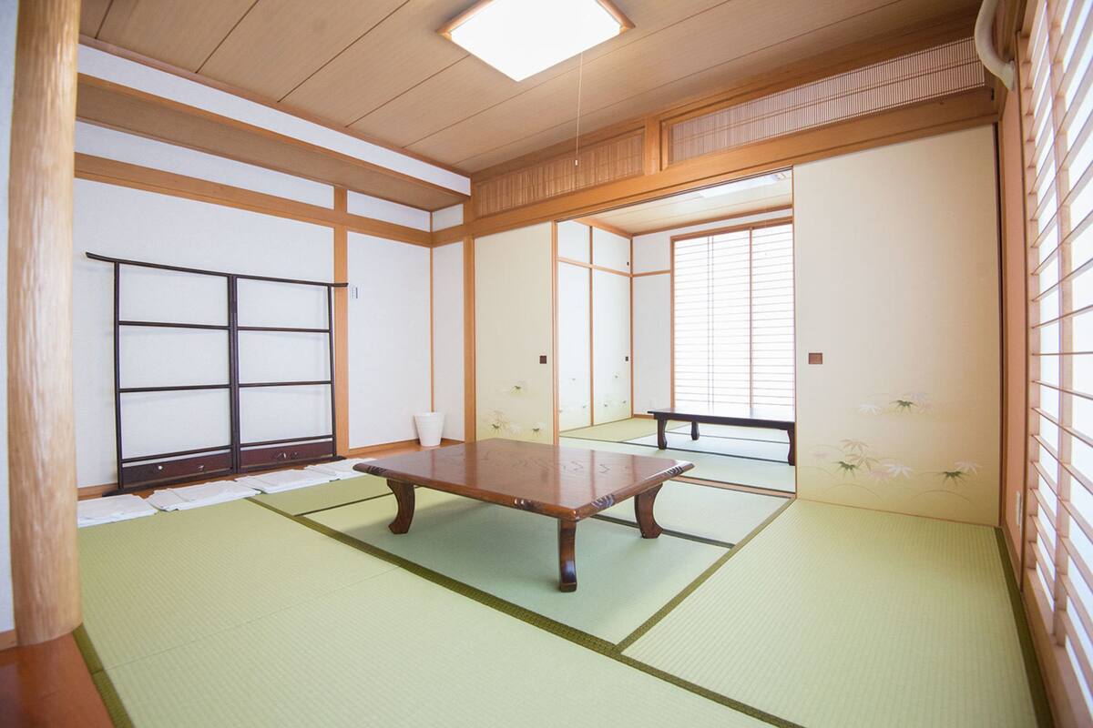 Um quarto japonês tradicional com tatames, uma mesa de madeira baixa, portas deslizantes e uma vista pela janela.