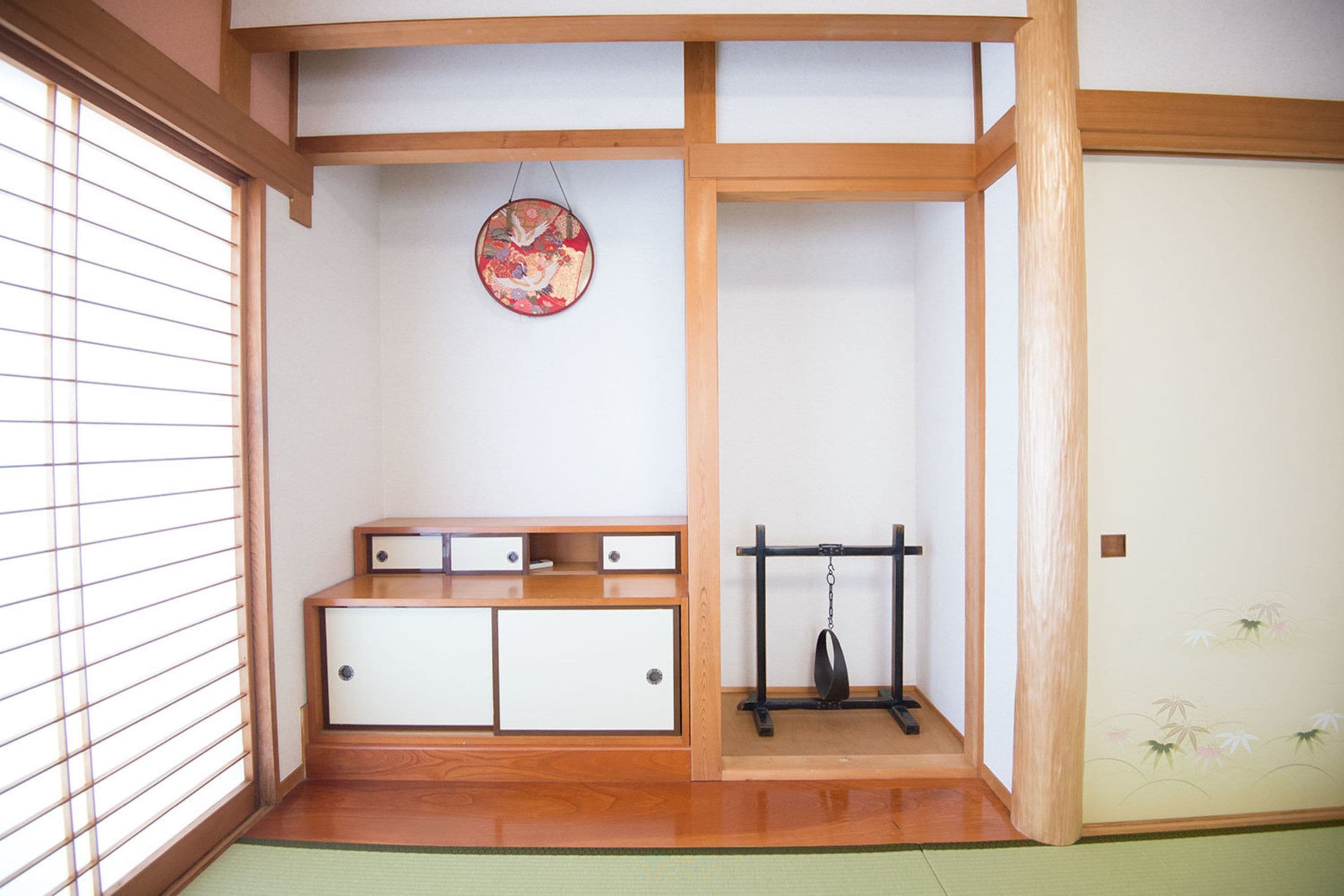 Una habitación japonesa tradicional con suelo de tatami, un panel shoji, un mueble de madera bajo y un adorno colgante.