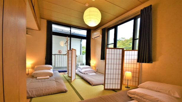 A traditional Japanese-style hotel room with tatami flooring, a shoji screen, and a view of the outdoors.