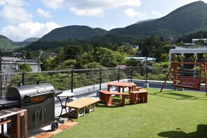 A rooftop patio with a barbecue grill, wooden tables, and a swing set.