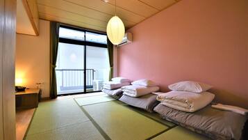 Quarto com tatames, futon com travesseiros, porta de vidro deslizante para uma varanda e um lanterna de papel suspensa.