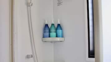 Zona de ducha con cabezal de ducha manual, grifo de pared y tres botellas de productos 'uminela' en una repisa.