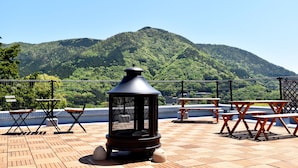 A terrace with a view of a forested mountain, outdoor seating, and a fire pit.