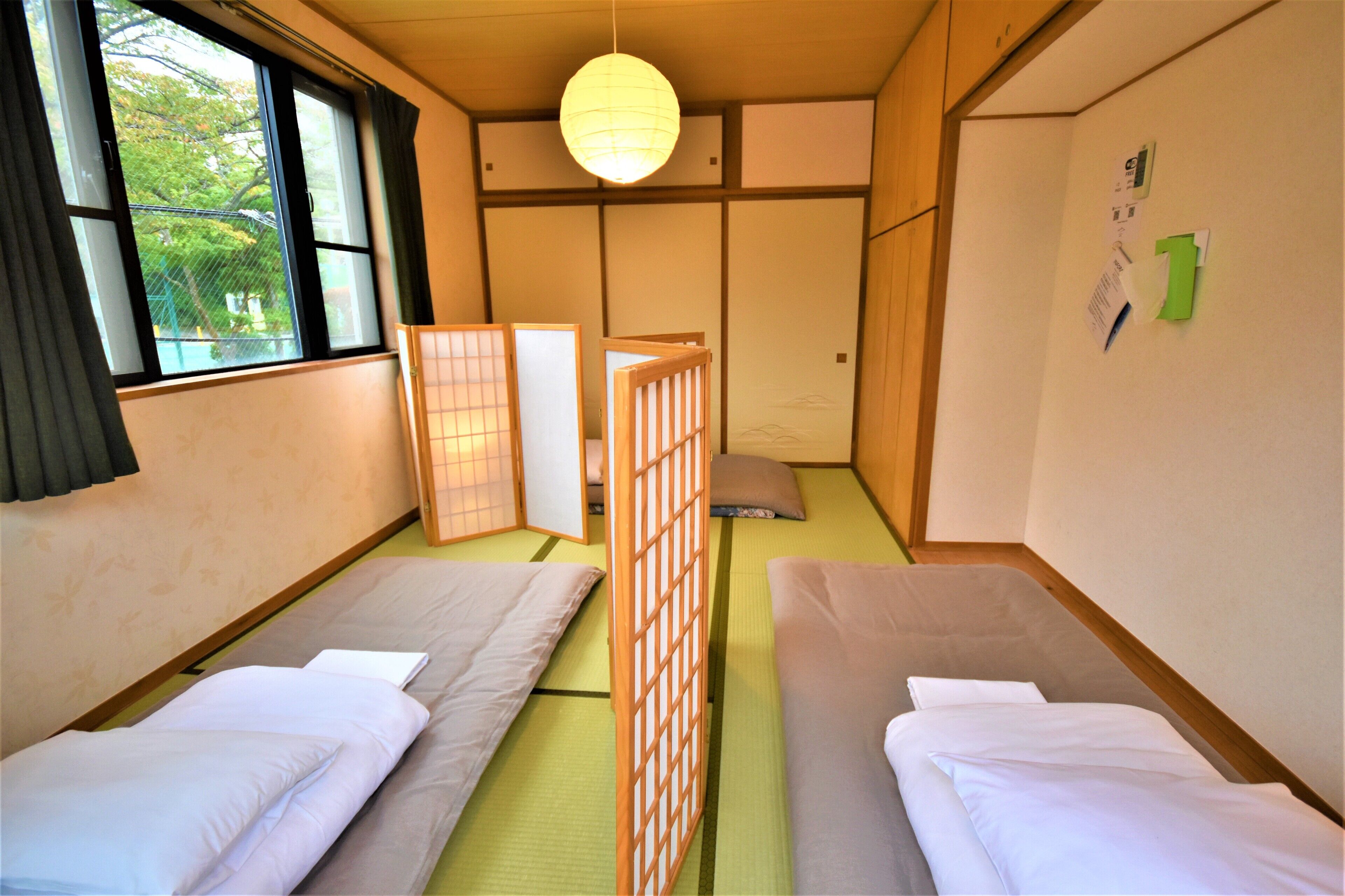 A traditional Japanese-style room with tatami flooring, two single beds, a shoji screen, and a hanging paper lantern.