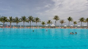 A large outdoor swimming pool with clear blue water, surrounded by palm trees and beach umbrellas. - Ambassador City Jomtien Pattaya - Garden Wing (Sattahip)