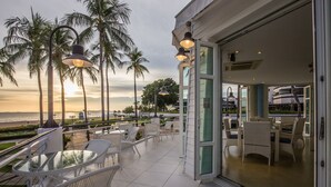 A balcony with white wicker furniture and a glass table, overlooking a beach and palm trees during sunset. - Ambassador City Jomtien Pattaya - Garden Wing (Sattahip)