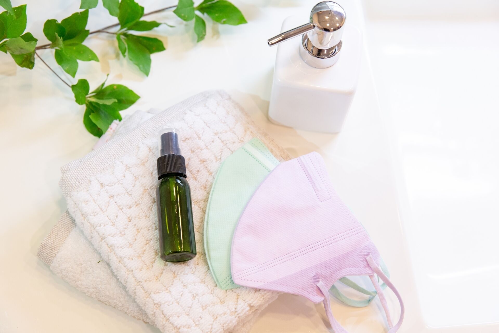 Un lavamanos con una botella verde, una mascarilla rosa y un dispensador de jabón blanco.
