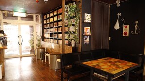 A cozy cafe with wooden flooring, a central table with chairs, a bookshelf, and decorative wall art.