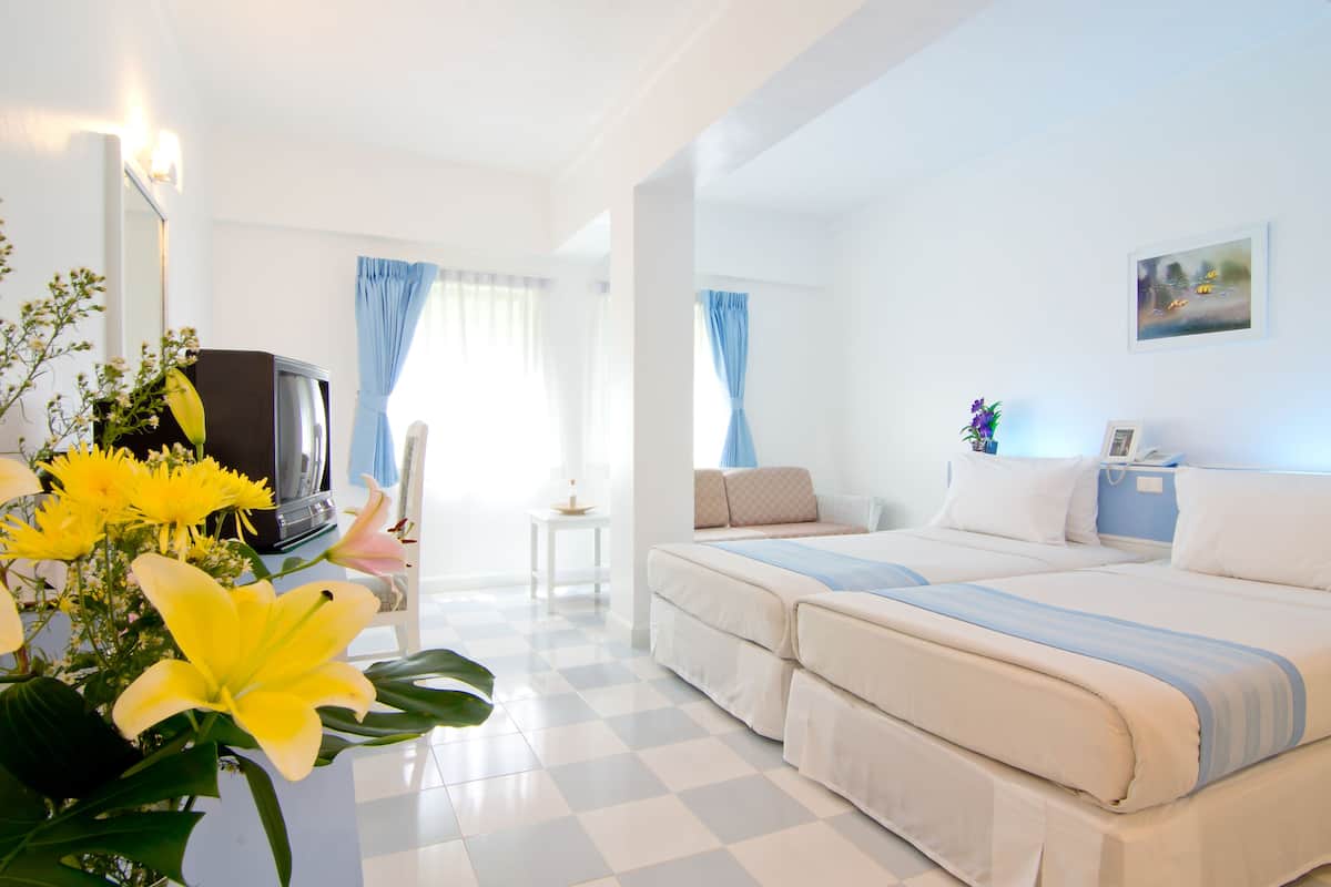 Une chambre d’hôtel avec deux lits, une télévision, une petite table et un vase de fleurs.