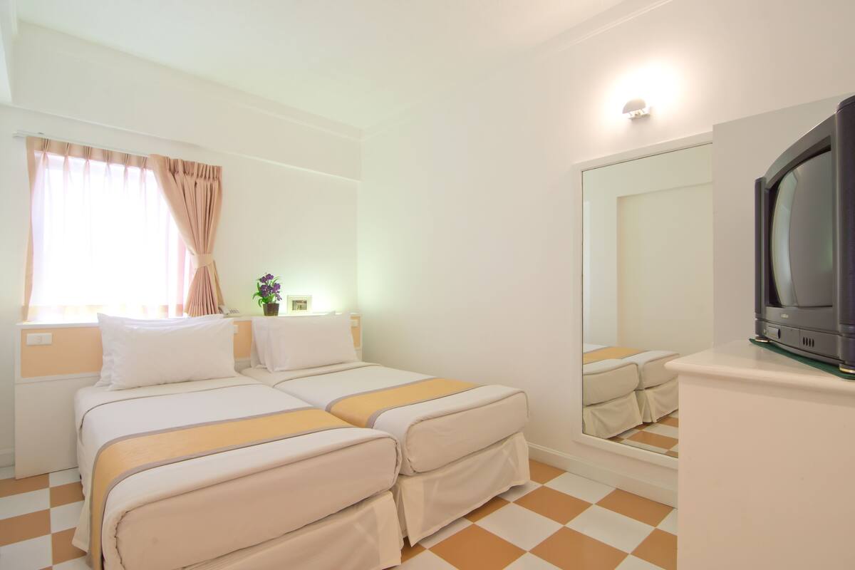 Une chambre d’hôtel avec deux lits, une télévision, un grand miroir et un sol à carreaux.