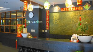 Un área de recepción con un mostrador de madera, una planta grande en maceta, decoraciones chinas tradicionales y una lámpara de araña moderna.