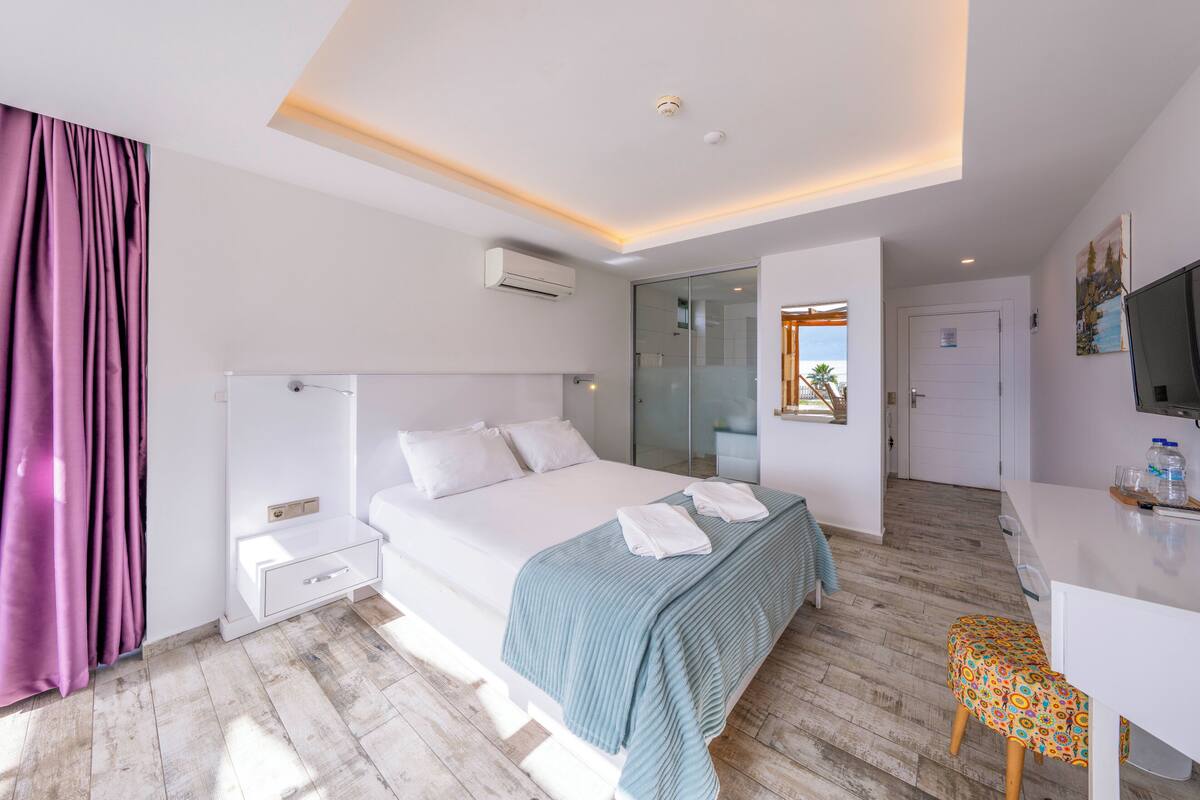 A modern hotel room with a bed, bedside table, and a desk with a chair.