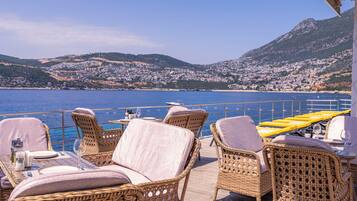 Una terraza con mobiliario de mimbre y una mesa lista para comer, con vistas a un pueblo costero y al mar.