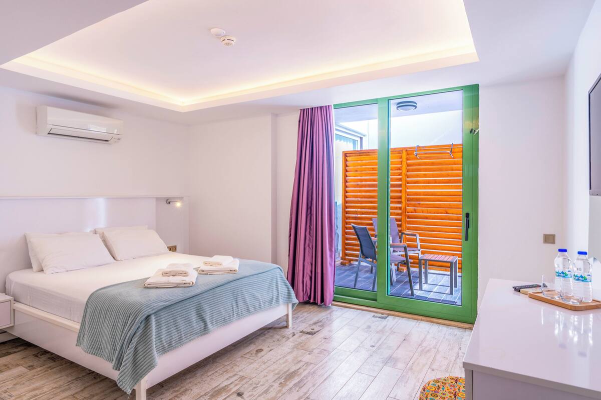 A modern bedroom with a bed, a desk with a chair, and a sliding glass door leading to an outdoor area.