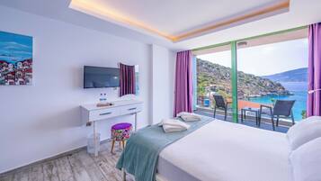 A hotel room with a bed, a desk with a TV, a small stool, and a view of the sea.