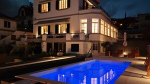 Una casa moderna de dos pisos con piscina, mobiliario exterior y una escalera que lleva al piso superior.
