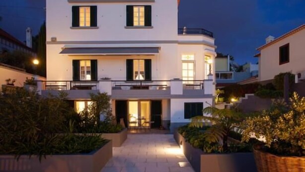 Una casa moderna de dos pisos con un balcón, un porche cubierto y un jardín bien iluminado.