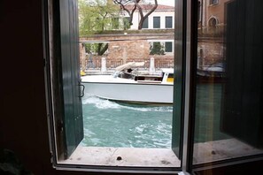 Vista a través de una ventana de un canal, con un barco y edificios al fondo.