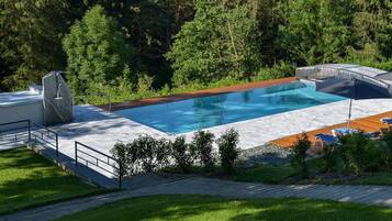 Ein Schwimmbecken mit Holzterrasse und Liegestühlen, umgeben von Grünpflanzen.