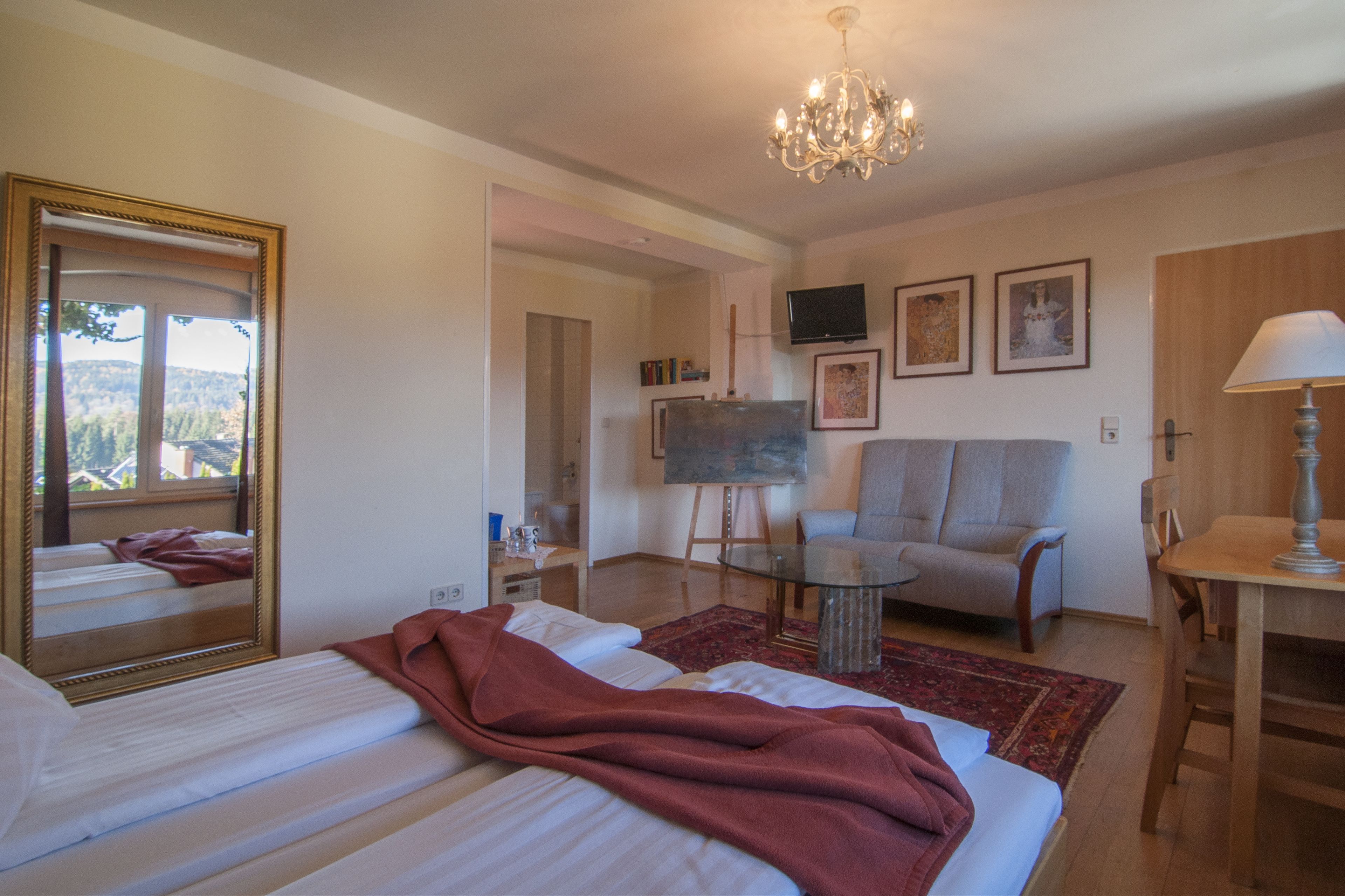 Quarto de hotel com cama, sofá, mesa de jantar, lustre e obras de arte nas paredes.