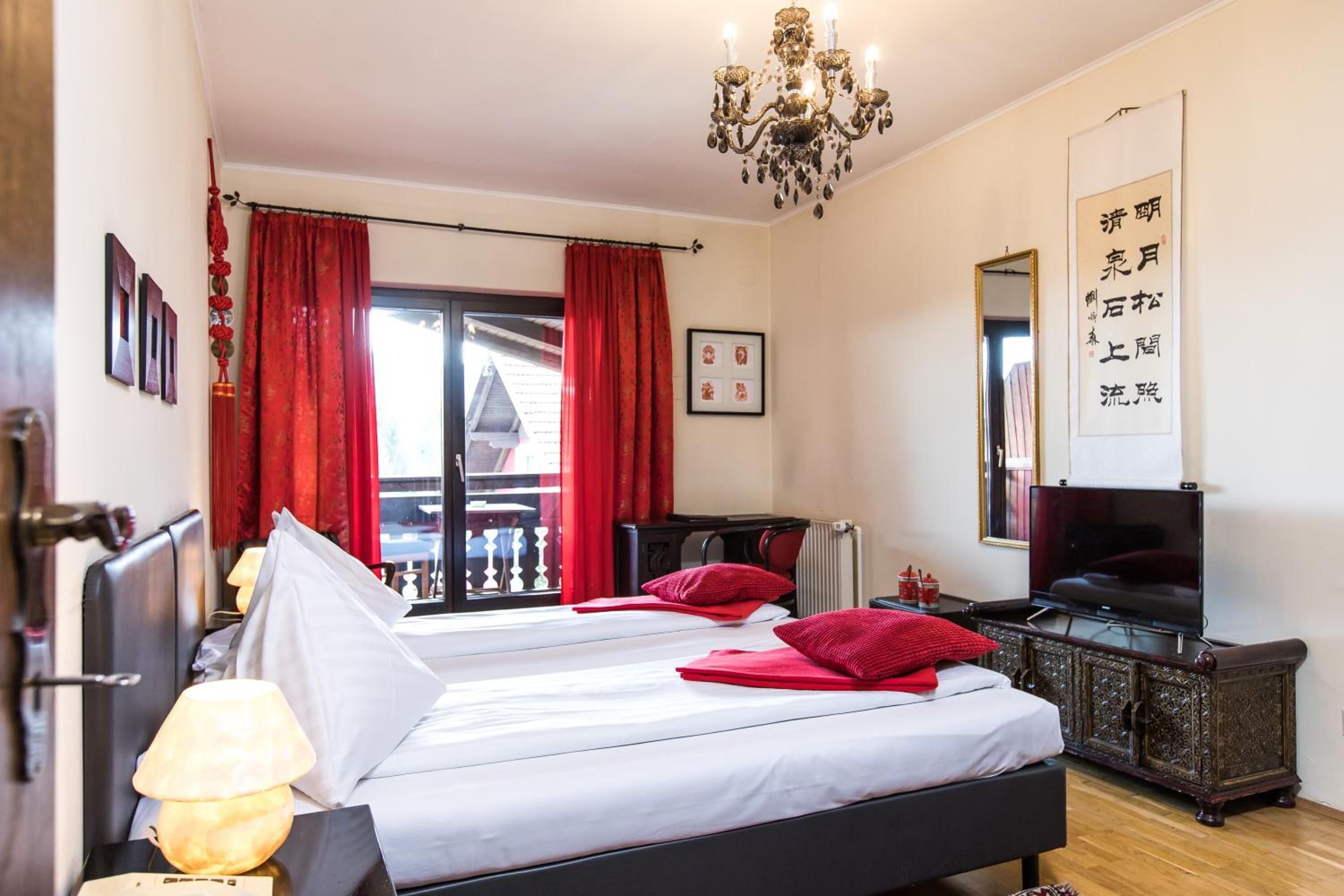 Habitación de hotel con cama, televisor, escritorio y balcón con cortinas rojas.