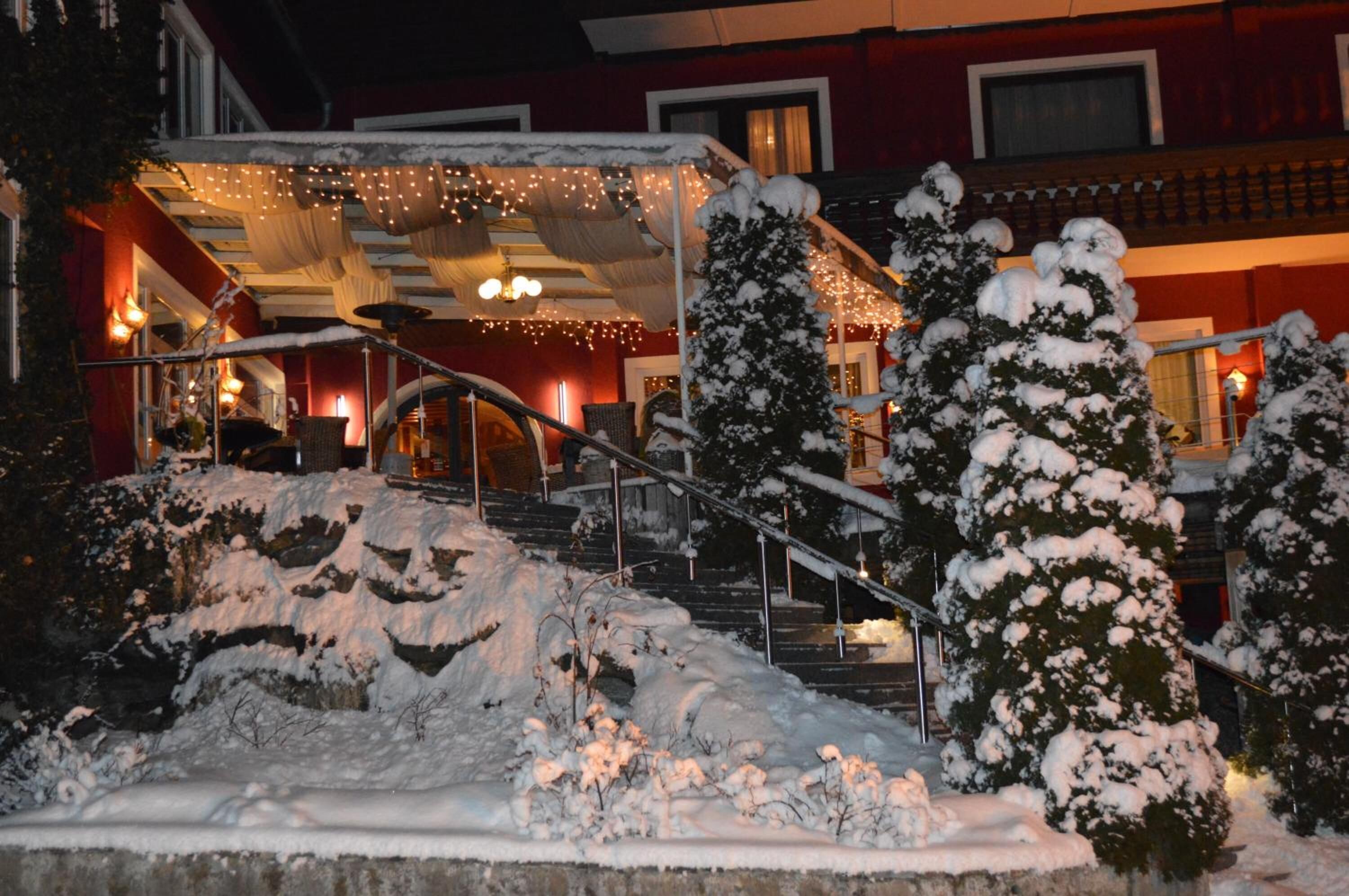L’entrée d’un hôtel, avec un escalier et des arbres couverts de neige, illuminés par des guirlandes lumineuses.