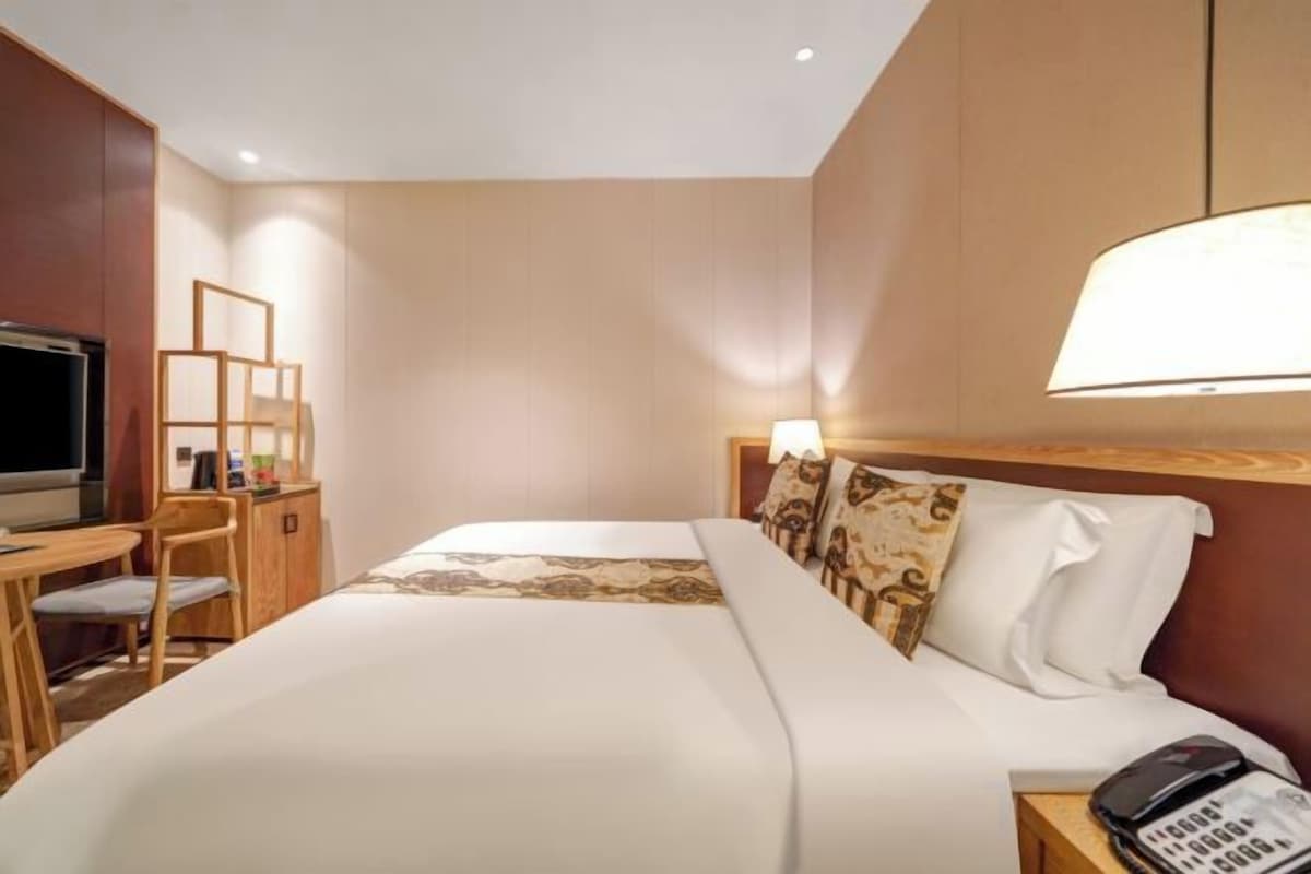A hotel room with a bed, a desk with a chair, a television, and a lamp.