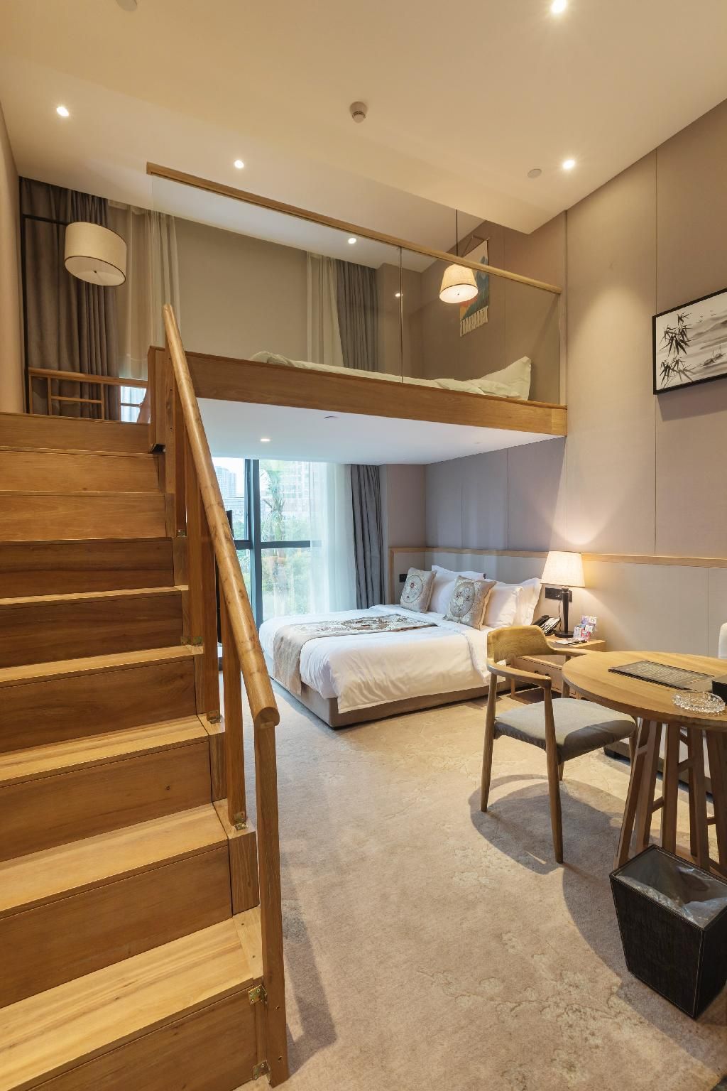 Een hotelkamer met een stapelbed, een houten trap, een bureau met stoel en een nachtkastje.