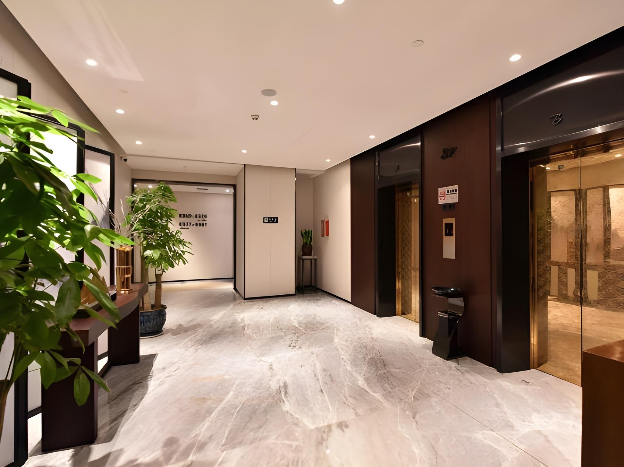 A modern hotel lobby with a marble floor, a reception desk, and a plant.