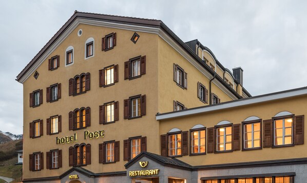 Un immeuble à plusieurs étages, doté d’une façade jaune, de nombreuses fenêtres avec des volets en bois et d’une enseigne indiquant qu’il s’agit d’un hôtel et d’un restaurant.